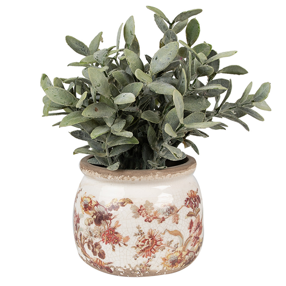 Un pot de fleurs en céramique au style vintage, décoré d’un motif floral délicat dans des tons rouges, jaunes et verts sur un fond blanc patiné. Il contient une plante artificielle aux feuilles vertes légèrement poudrées, apportant une touche naturelle et élégante. Le bord supérieur du pot présente une finition vieillie, renforçant son charme rustique.